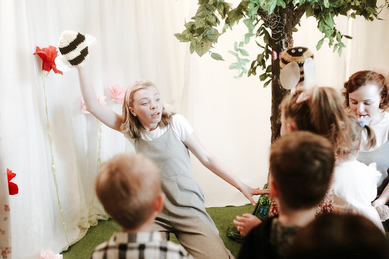 About Group of children watching a lively puppet performance indoors with nature decor.